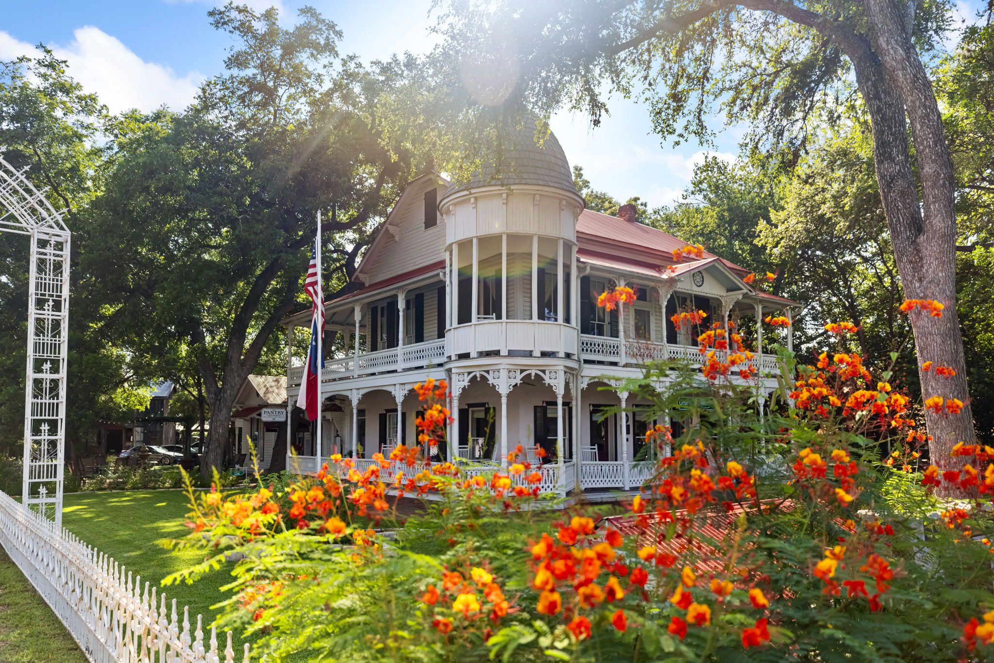 Victorian-style house with large porch, surrounded by trees and bright orange flowers in the garden.
